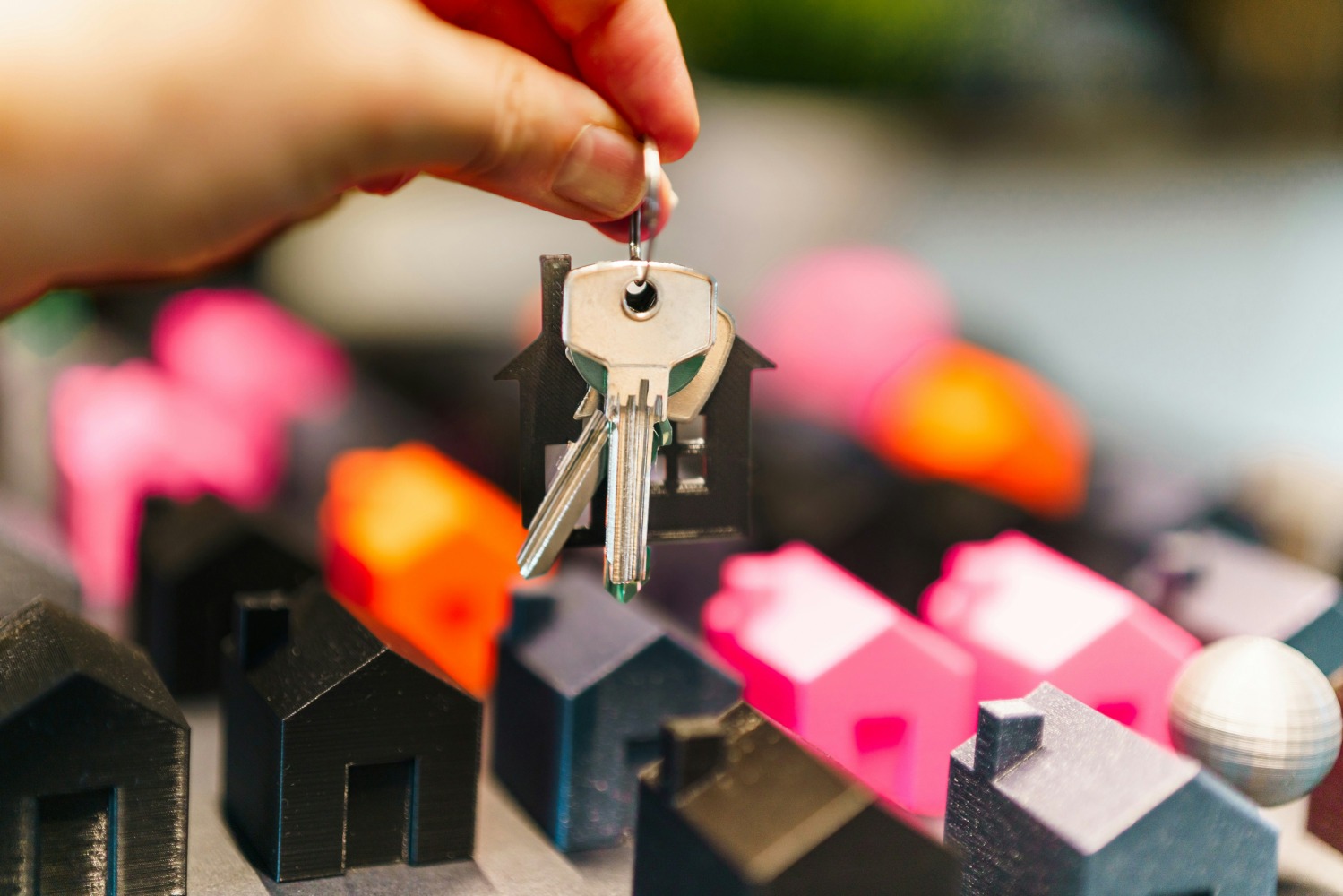Set of keys being held above miniature plastic houses